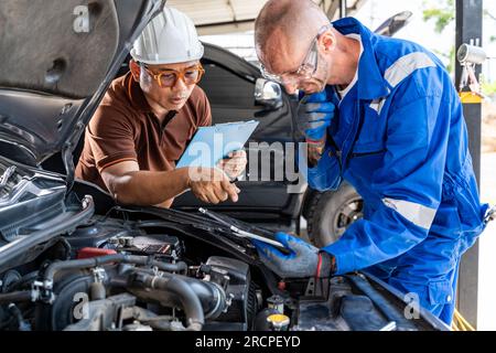Two male auto mechanics working together on the car engine at their car repair garage Stock Photo