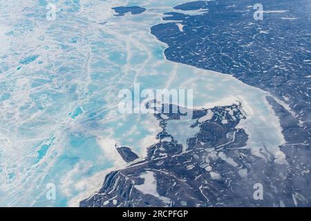 Aerial view from 38,000 feet of the flat landscape on the coastline of Greenland in the Arctic circle mostly covered in snow and low clouds hanging on Stock Photo