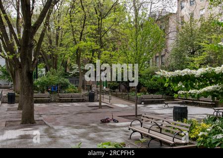 New York City, NY, USA-June 2022; View over a typical neighborhood playground in Manhatten with equipment and surrounded by trees and park benches; on Stock Photo
