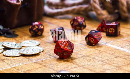 low angle shot featuring a collection of vibrant red RPG dice and golden gaming coins arranged on a battle map Stock Photo