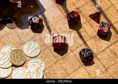 Overhead shot featuring a collection of vibrant red RPG dice and golden gaming coins arranged on a battle map Stock Photo