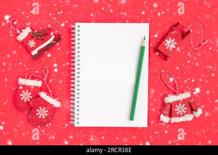 Christmas presents preparation. Notebook, pencil, decorative snowflakes, mitten, sledge, skates on red background. Xmas and Happy New Year composition Stock Photo