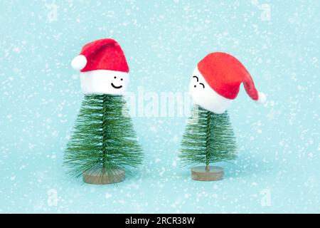 Two small Christmas trees in red Santa Hats. Decorating of Artificial Fir tree. Beautiful imitation of a mini Christmas tree, with Santa Cap on blue b Stock Photo
