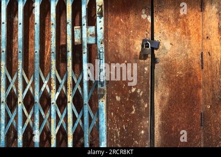 Old gold steel lock and damaged and rusted steel door on wooden door. Locked on wooden door with old steel metal shutter and folding door gate. Old wo Stock Photo