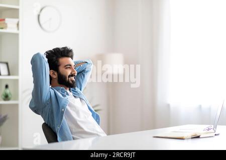 Smiling Relaxed Eastern Man Leaning Back In Chair At Home Office Stock Photo