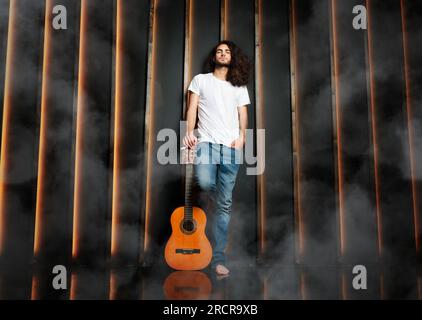 Man With Guitar Standing Leaning On Black Wall In Studio Stock Photo