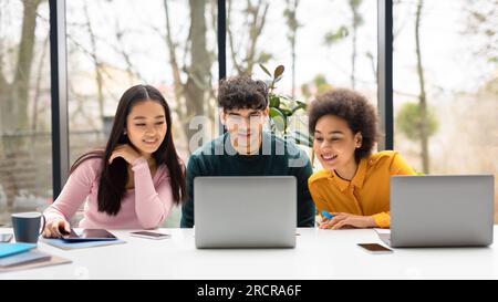 Studying together. Three international students sitting at desk in auditorium using laptop, watching educational video Stock Photo