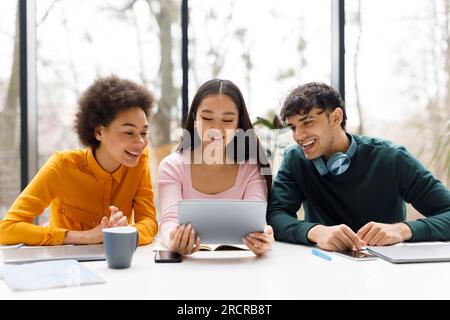 Group of diverse smart university students sitting in classroom discussing and working on project together, using tablet Stock Photo
