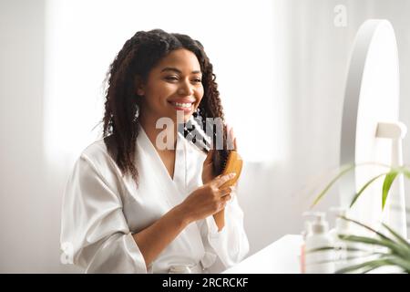 Smiling Young Black Woman Brushing Her Beautiful Hair With Comb At Home Stock Photo