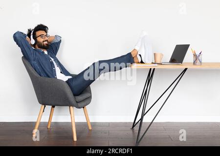 Relaxed young arab guy using laptop and headphones at office Stock Photo
