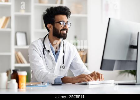 Arab man general practitioner look at computer screen, consult patient Stock Photo