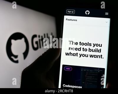 Person holding smartphone with website of US software development company GitHub Inc. on screen with logo. Focus on center of phone display. Stock Photo