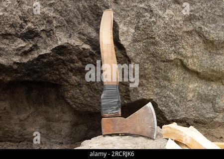 An old working ax lies on a granite stone in the summer in the forest while chopping firewood, a tool for chopping firewood, a lumberjack Stock Photo
