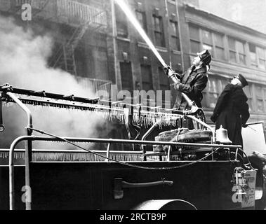 New York, New York:  c. 1935 New York City fire men putting a hose on a fire on West 13th Street in freezing temperatures. Stock Photo