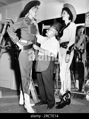 Hollywood, California:  August 20, 1958 Two six foot, three inch tall women are fitted in cowboy gear by a short tailor for promoting the film, 'The Big Country'. The women are members of the local 'Tip Toppers' organization. Stock Photo