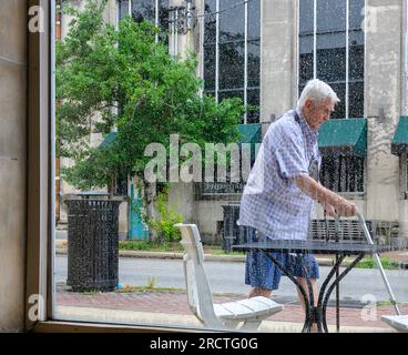NEW ORLEANS, LA, USA - JULY 12, 2023: Male senior citizen using two canes to walk past window of cafe on Oak Street in Uptown Neighborhood Stock Photo
