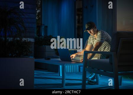 Caucasian Man in His 40 Doing His Remote Computer Work Inside His Back Yard Garden. Working on His Laptop. Stock Photo