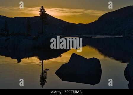 Mountain, tree and boulder at sunset with their reflection in Aloha Lake. Stock Photo