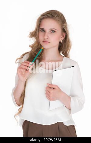 Thoughtful blonde woman secretary holding white clipboard in hand, green pencil in other hand near chin. Well-dressed Caucasian female in white blouse Stock Photo