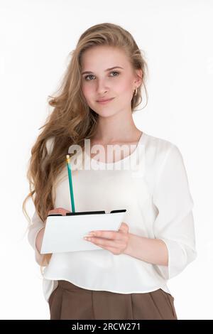 Portrait of businesswoman looking at camera, writes on clipboard with pencil. Well-dressed Caucasian young adult female in white blouse Stock Photo
