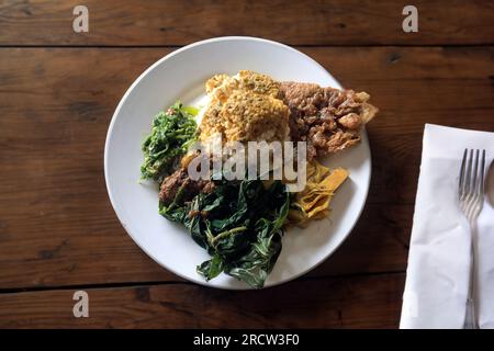 Nasi Padang consisting of white rice, rendang, egg, vegetables in a white plate. Indonesian traditional food. Rendang Padang Stock Photo