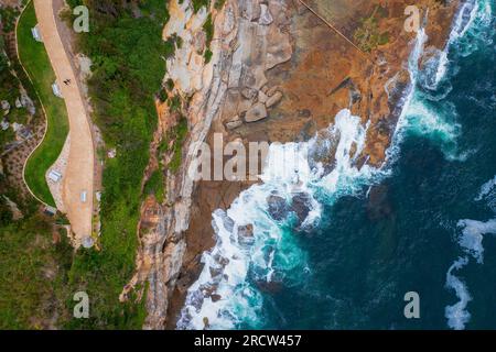 Aerial drone view of a rocky coast line Dee Why NSW Sydney Australia. People resting and walking on a footpath and rocks. Stock Photo