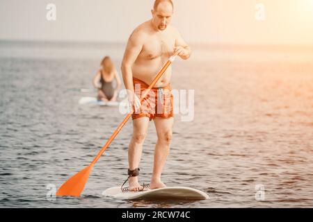 Active mature male paddler with his paddleboard and paddle on a sea at summer. Happy senior man stands with a SUP board. Stand up paddle boarding - Stock Photo