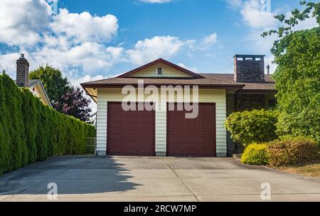 Double garage with short driveway in a sunny summer day. A perfect neighborhood. Family house with wide garage door and concrete driveway in front. A Stock Photo