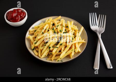 Garlic French Fries with Parsley on a Plate on a black background, side view. Stock Photo