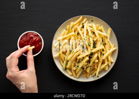 Female hand takes Garlic French Fries with Parsley, top view. Overhead, from above, flat lay. Stock Photo