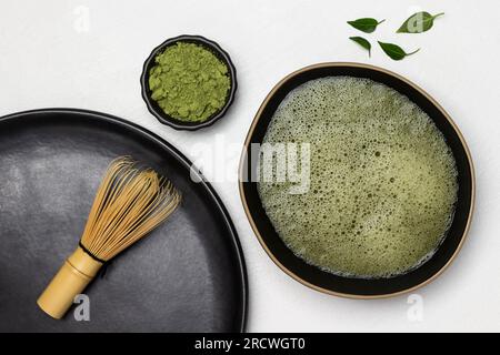 Bamboo whisk on a black plate. Matcha tea in a black bowl. Green matcha tea powder in a bowl. Flat lay. White background Stock Photo