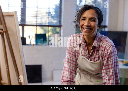 Portrait of happy biracial woman wearing apron in home studio Stock Photo