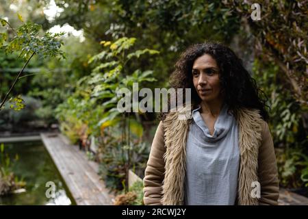 Happy biracial woman with dark curly hair smiling in garden Stock Photo