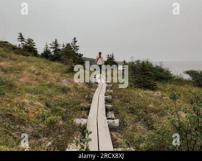 Woman walking along wooden path on Newfoundland coastline. Stock Photo