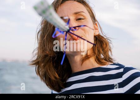 Middle-aged brunette woman in stripes blowing a party favor Stock Photo
