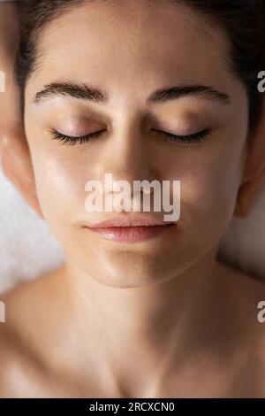 Close-up of a woman lying on a massage table with her eyes closed getting ready for procedures. Spa skin and body care. Facial beauty treatment Stock Photo