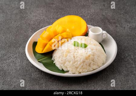 Delicious Thai mango sticky rice with cut fresh mango fruit in a plate on gray table background. Stock Photo