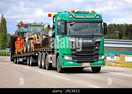 Green Scania R650 truck transports roadworks asphalting machinery on flat trailer along highway 52. Salo, Finland. July 7, 2023. Stock Photo
