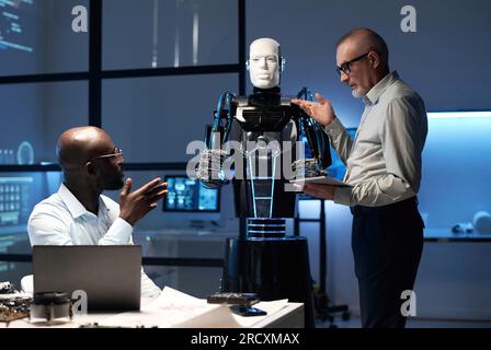 Engineers discussing designing of robot in team during their work in laboratory Stock Photo