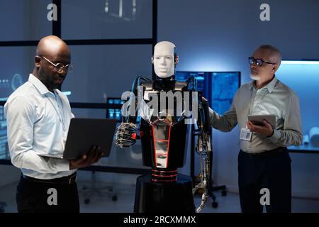 Engineers using gadgets to connect robot during their teamwork in the laboratory Stock Photo