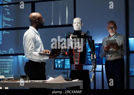 Engineers programming cyborg robot with gadgets in office Stock Photo