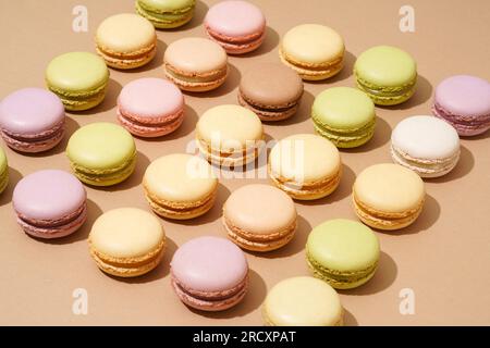 An overhead shot of a beige table surface featuring an array of colorful macarons in neat rows Stock Photo