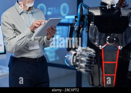 Close-up of mature engineer using digital tablet to connect with robot during his work in the lab Stock Photo