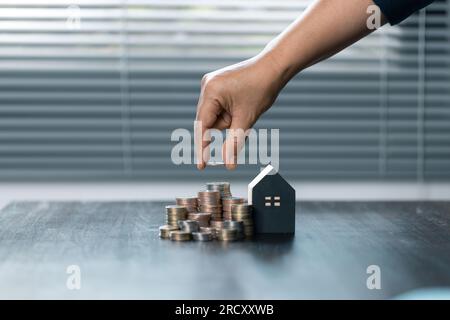 Saving money for house and real estate. Woman hand protecting on stack coins and house model on table. Stock Photo