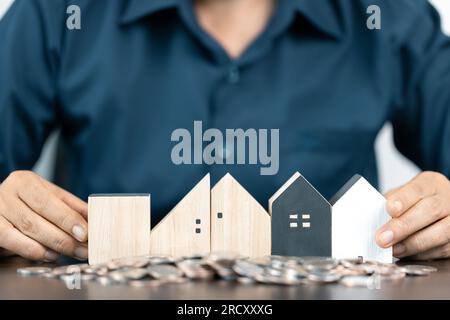 Saving money for house and real estate. Woman hand protecting on stack coins and house model on table. Stock Photo