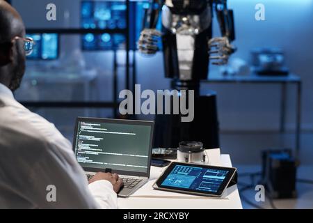 Rear view of engineer typing security codes on laptop to develop robotic industry Stock Photo