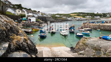 COVERACK, CORNWALL, UK - JUNE 27, 2023.   Landscape view of traditional Cornish fishing boats moored in the tidal harbour of the picturesque fishing v Stock Photo