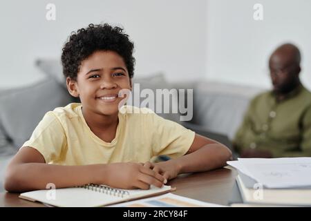 Portrait of African American boy smiling at camera while sitting at table and doing homework Stock Photo