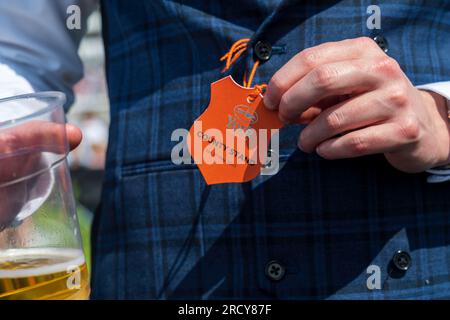 York horse race, a well-dressed man in an English style suit shows his pass for the York racecourse and his beer, during a popular horse racing event. Stock Photo