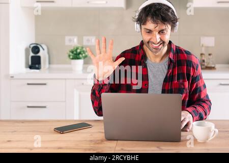 Smiling male student waving hand during video call on laptop at home Stock Photo